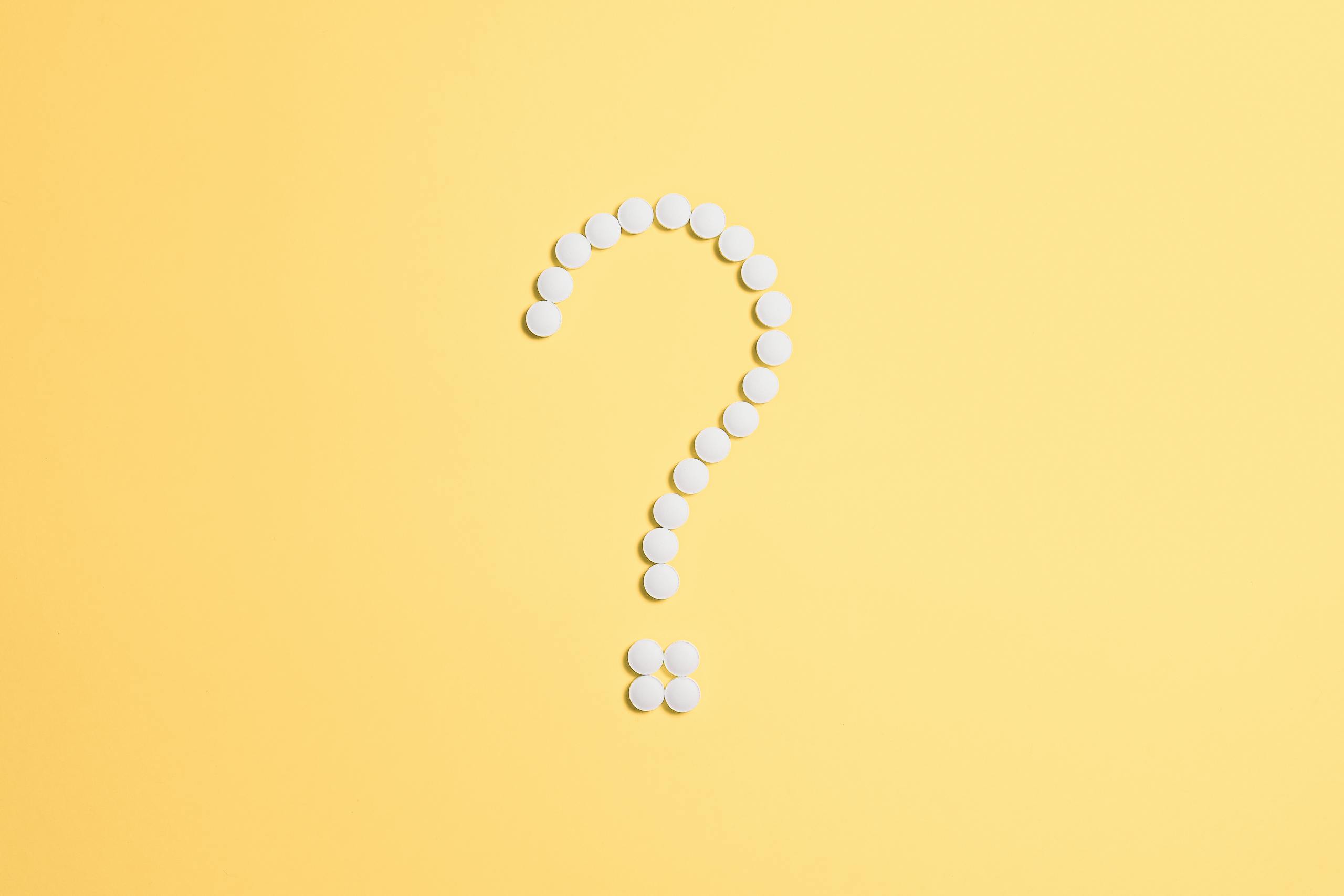 White pills arranged into a question mark shape on a vibrant yellow background.